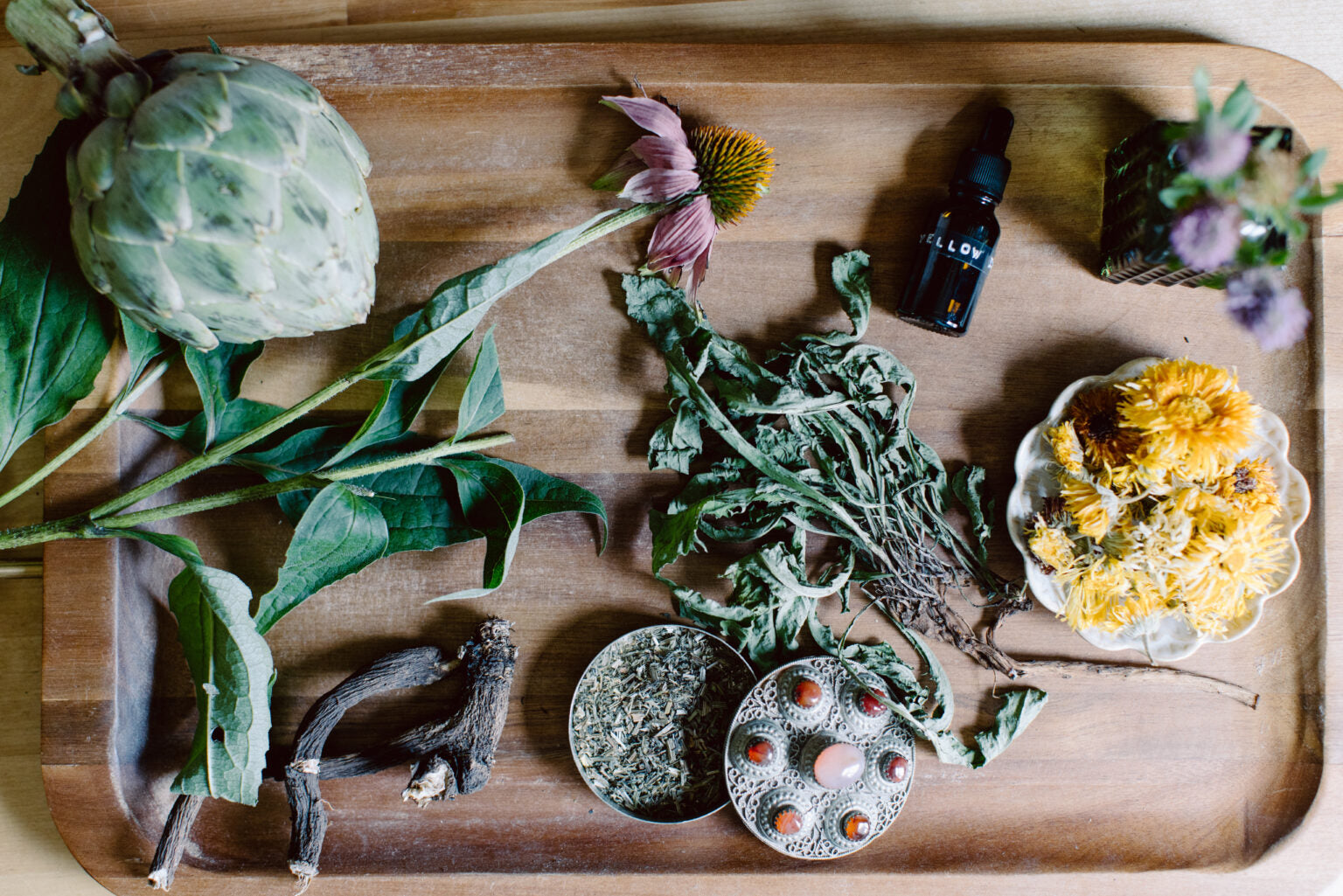 Wooden tray with herbs, flowers, and small objects on a wooden surface
